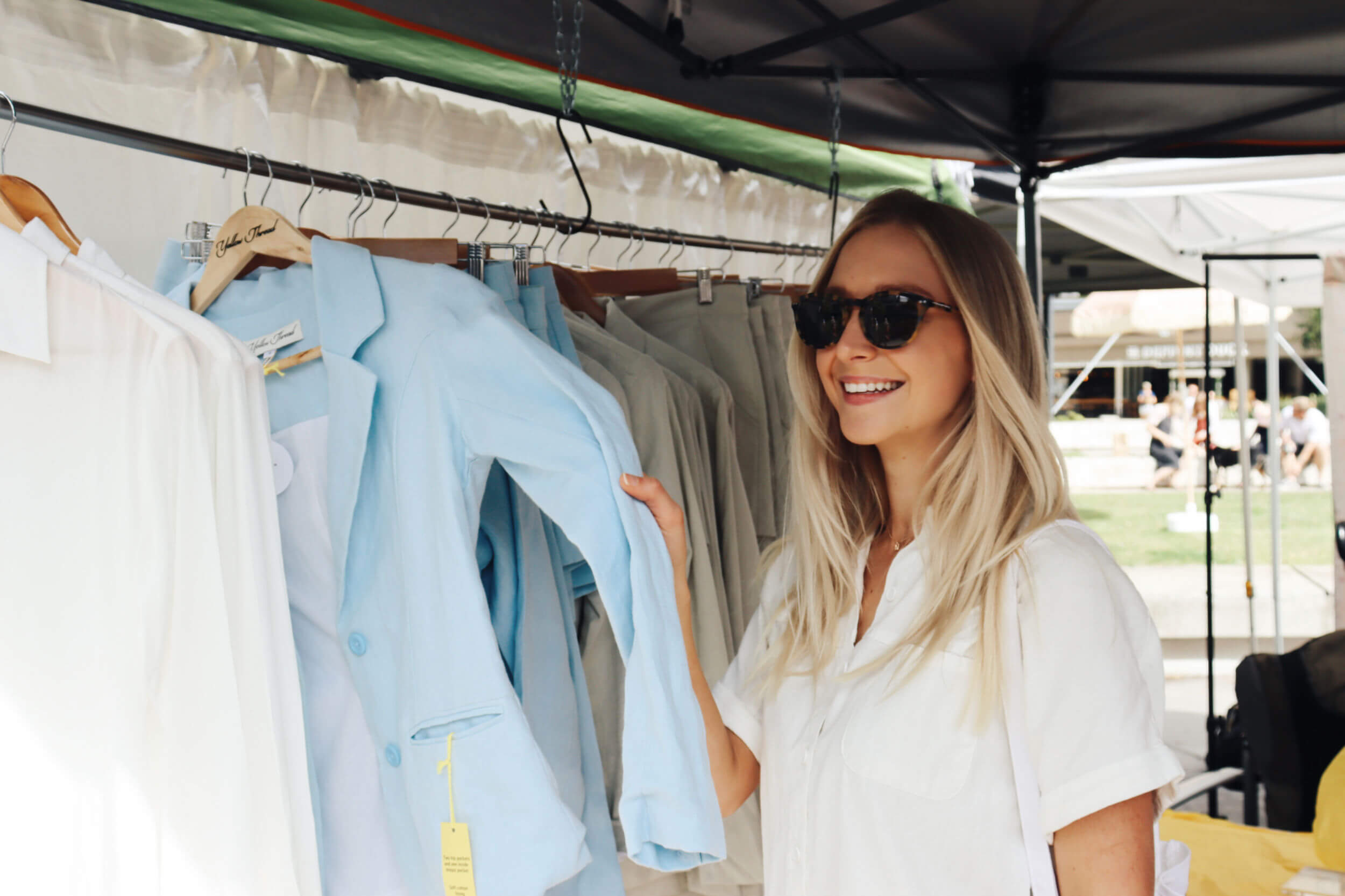 Lady browsing clothing apparel in Brisbane Markets by The Market Folk. she is holding a pale blue jacket.